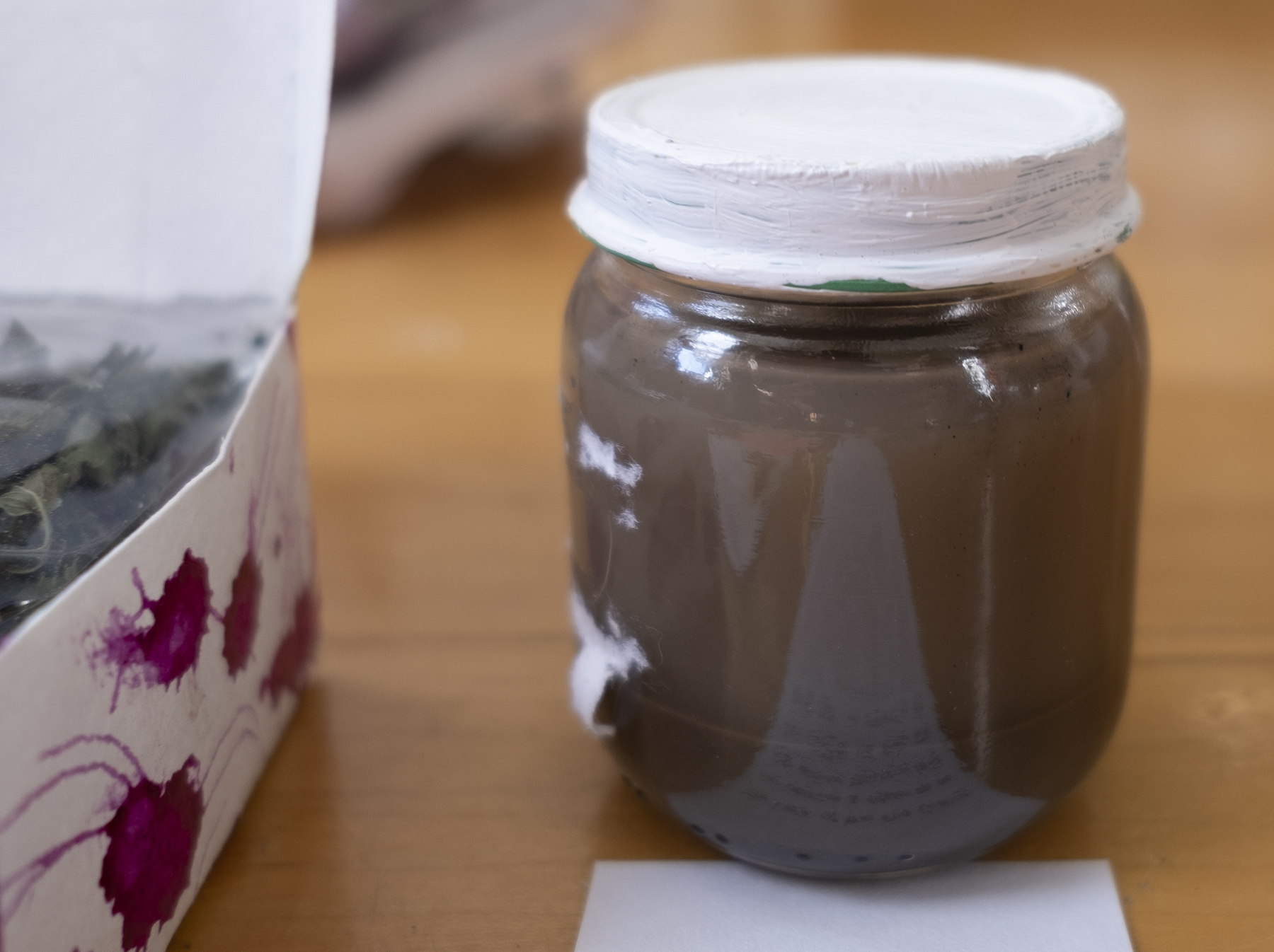 A jar of  murky brown water on a wood floor